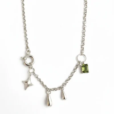 گردنبند نقره دست‌ساز با زنجیر ظریف، دارای آویز ستاره، قطره‌های سیمین و یک تک‌سنگ سواروسکی سبز در گوشه کار، عکاسی شده روی زمینه سفید