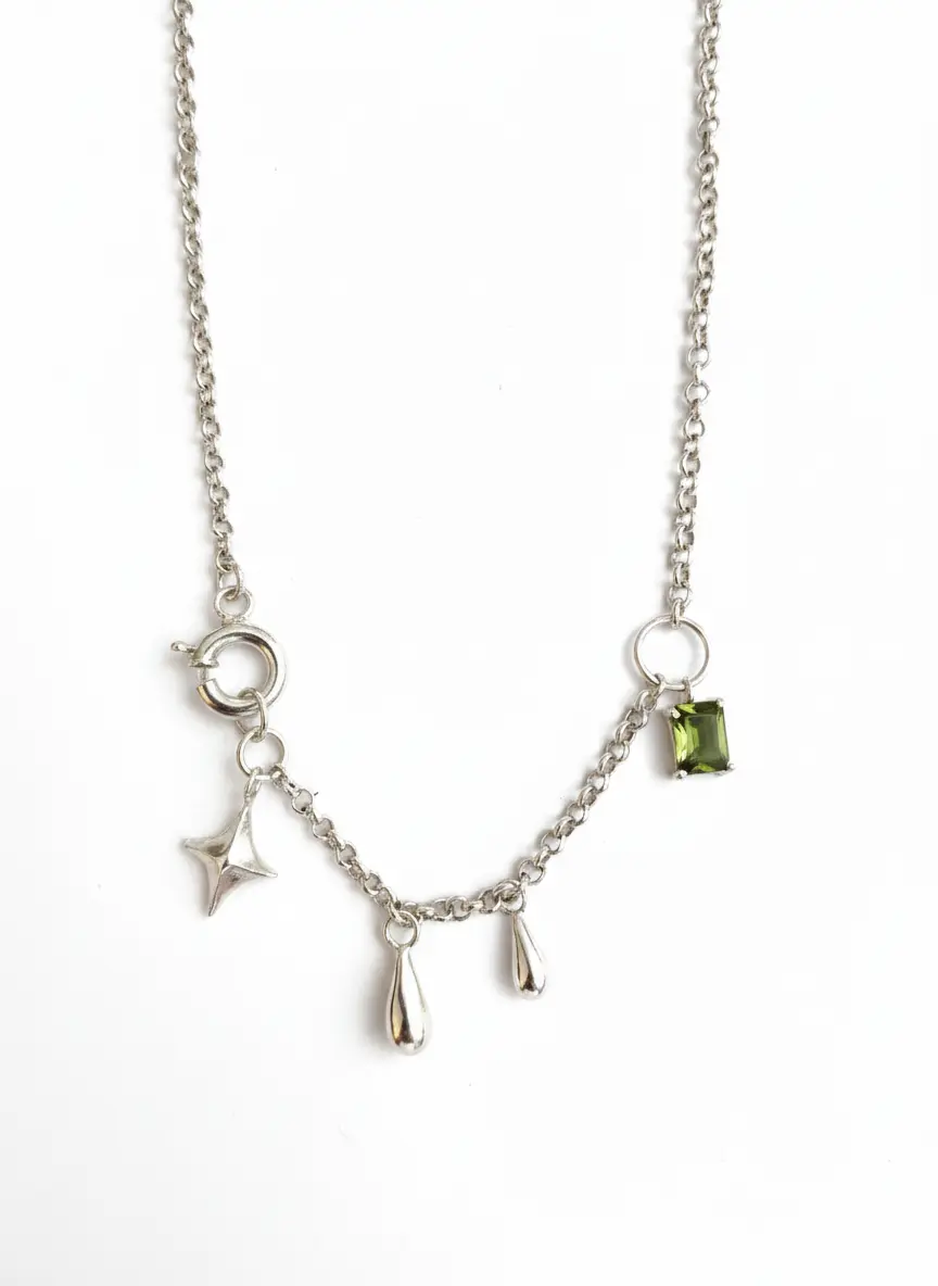 گردنبند ستاره و سنگ گردنبند نقره دستساز با زنجیر ظریف، دارای آویز ستاره، قطرههای سیمین و یک تکسنگ سواروسکی سبز در گوشه کار، عکاسی شده روی زمینه سفید