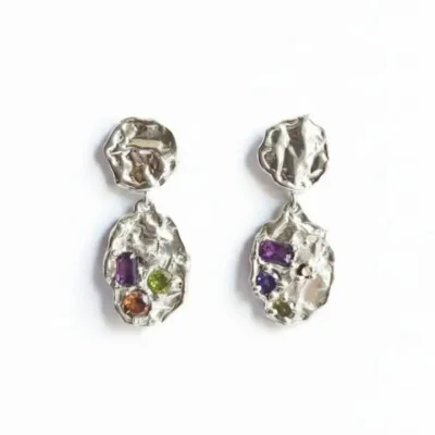 گوشواره‌های نقره دست‌ساز با سطح بافت‌دار و نامنظم دارای چهار سنگ اتمی درخشان به رنگ‌های بنفش، سبز و نارنجی، عکاسی شده روی زمینه سفید.