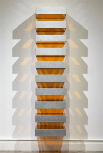 «چیدمان عمودی باکس‌های فلزی خاکستری با فضای داخلی نارنجی از دونالد جاد، ایجادکننده بازی نور و سایه روی دیوار.»