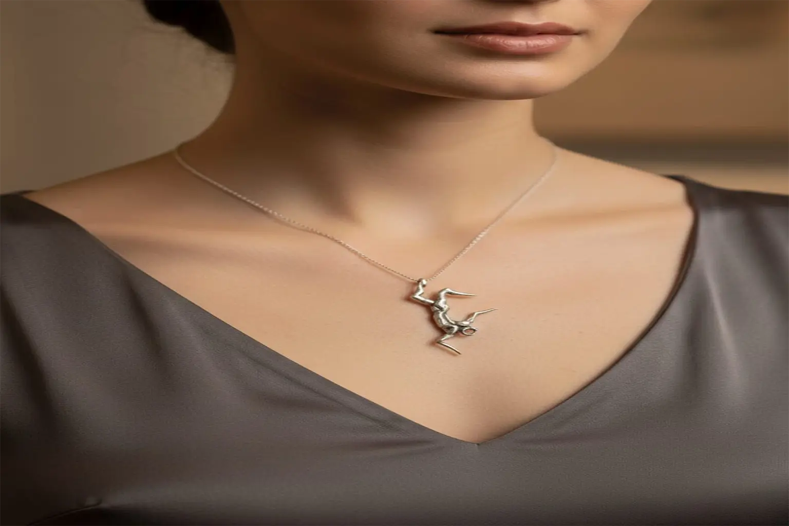نمای نزدیک از گردن و چانه یک مدل با لباس ساتن تیره که گردنبند نقره فیگوراتیو سقوط اثر سونا یداللهی را به گردن دارد.